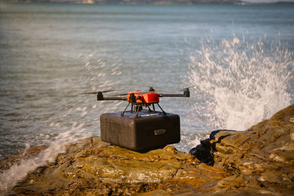 Perched on its carry case on rocks at the shoreline with waves splashing